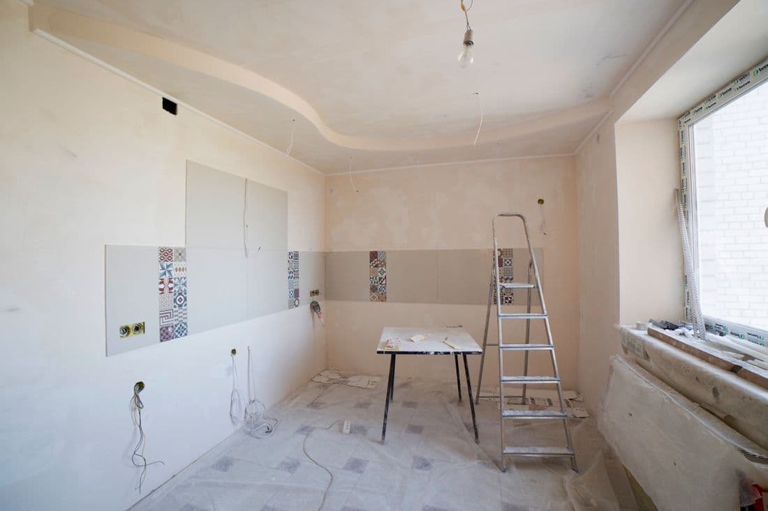 Cucina in ristrutturazione: intonaco fresco, fascia di cementine decorate e scatole elettriche a vista